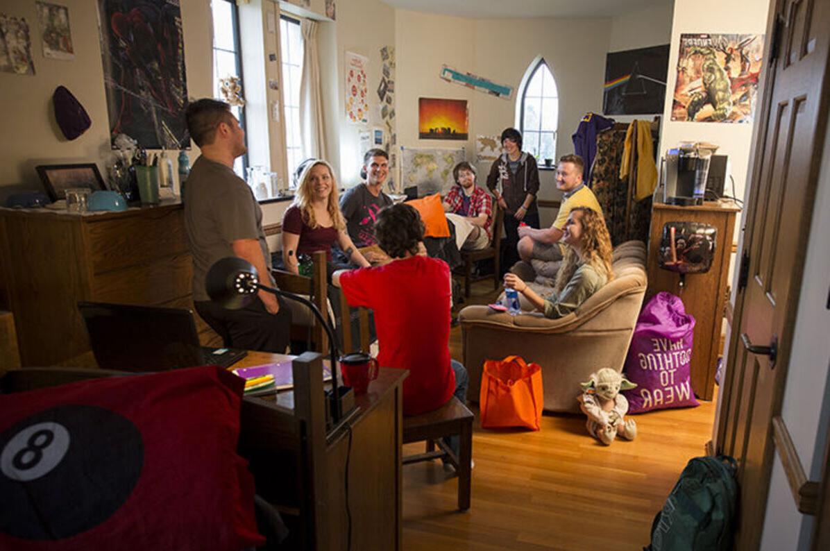 A group of eight students hang out and laugh in a dorm room